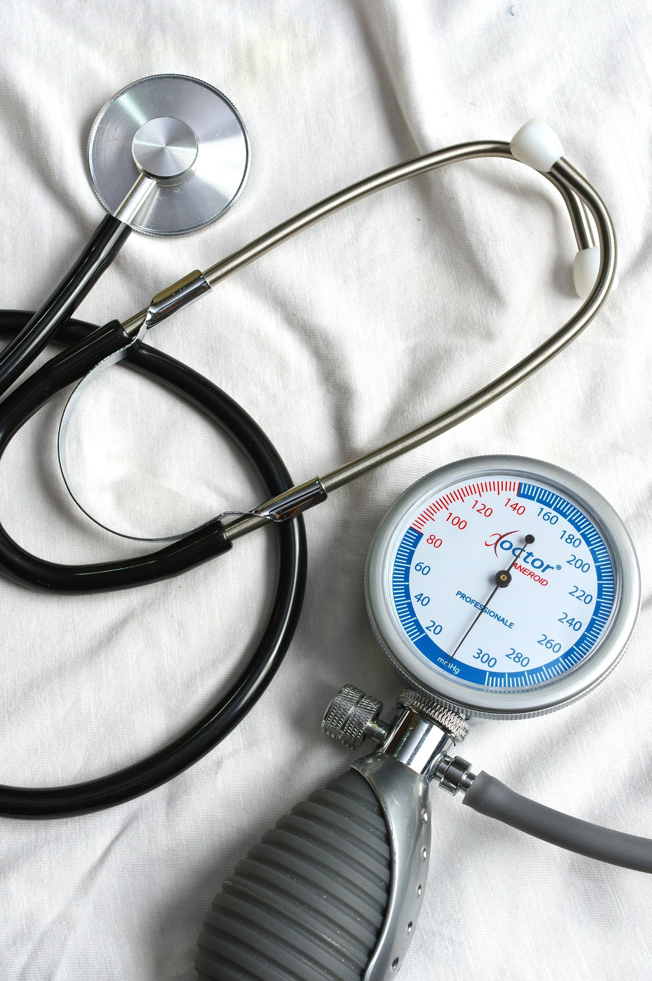A black stethoscope and a blood pressure gauge on a white fabric surface